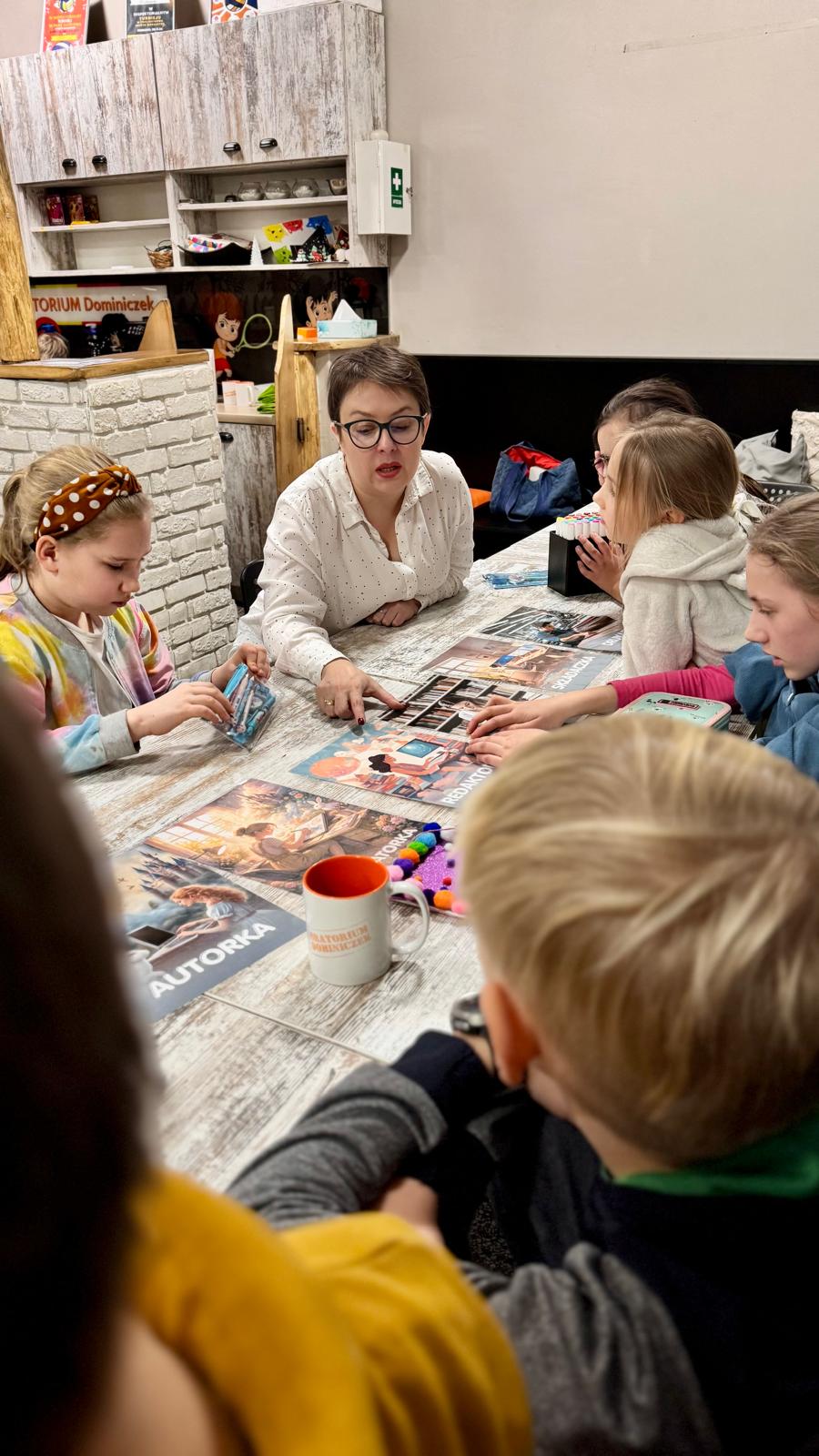 Katarzyna Bieńkowska siedzi z dziećmi przy stole z materiałami podczas spotkania
